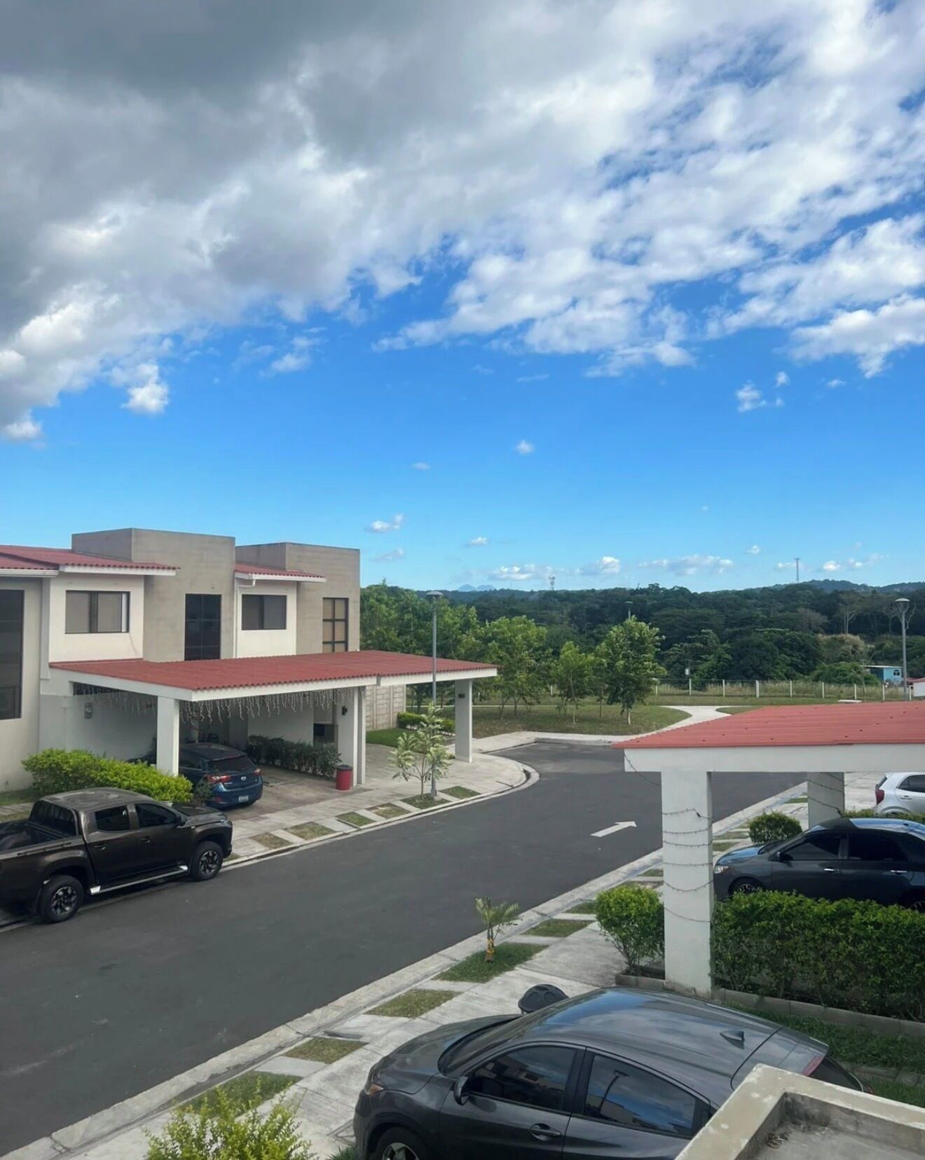 Un edificio moderno con zona de estacionamiento techada, una carretera que lo lleva y un paisaje montañoso al fondo.