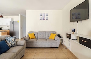 A living room with a sofa, a television, and a kitchen in the background.