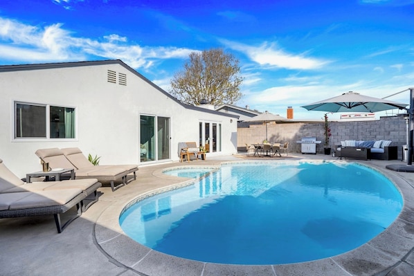 Una casa moderna con piscina, muebles de exterior y zona de barbacoa.