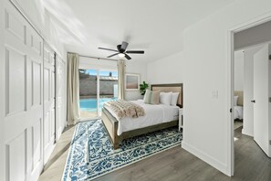 Un dormitorio con cama, ventilador de techo, vista a una piscina y una puerta que da a otra habitación.