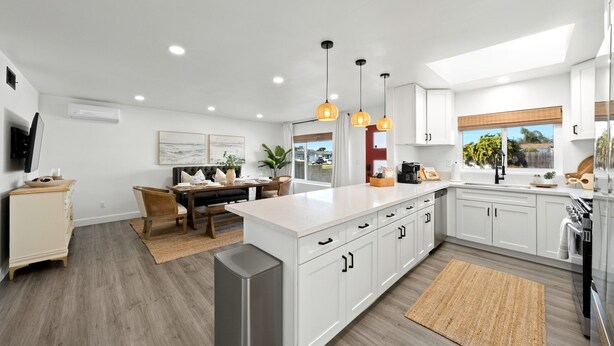 Una cocina moderna con armarios blancos, una isla central, luces colgantes y vistas al exterior.