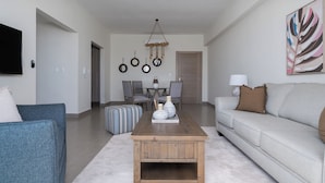 A modern living room with a wooden coffee table, a grey sofa, and a dining area with a chandelier. - Serenity in the Heart of Santo Domingo 80m2 Apartment Retreat (Santo Domingo)
