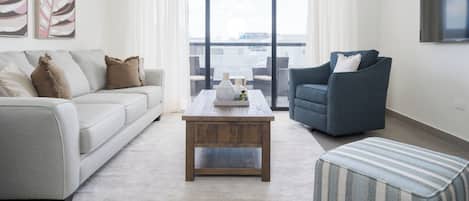 A modern living room with a sofa, armchair, coffee table, and a view through a large window.
