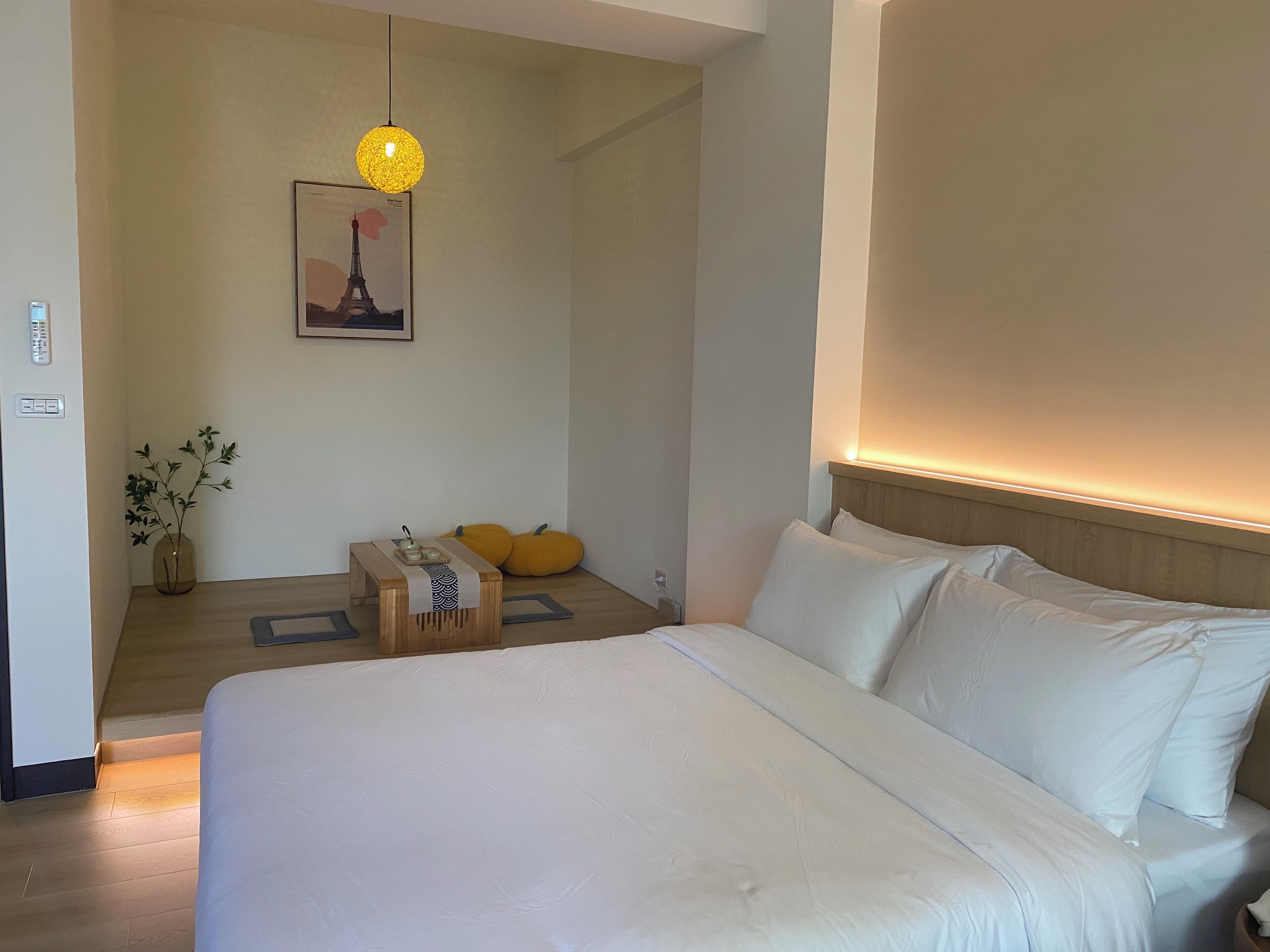 A hotel room with a large bed, a bedside table with a vase of flowers, a picture on the wall, and a hanging light fixture.