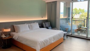 A hotel room with a large bed, a bedside table with a lamp, a chair, and a view of the outdoors through a sliding glass door. - Orange Homestay (Kaohsiung)
