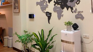 A room with a world map wall art, a water dispenser, and potted plants. - Orange Homestay (Kaohsiung)