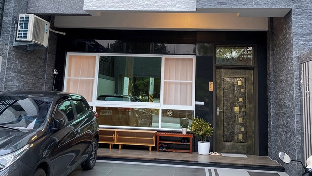 A modern building with a large glass window, a black car parked in front, and a potted plant near the entrance. - Orange Homestay (Kaohsiung)