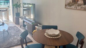 A modern living room with a round wooden dining table, blue upholstered chairs, a mounted flat-screen TV, a potted plant, and a large painting of a bull.