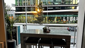 A modern building with a glass facade, a balcony with wicker furniture, and a potted plant.
