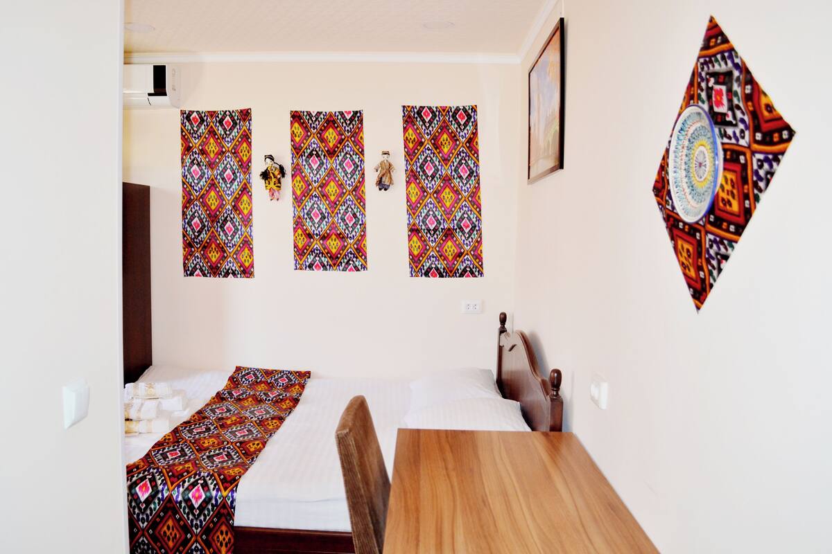 A room with a bed, a wooden table, and three patterned wall hangings.