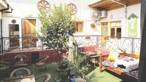 A courtyard with wicker furniture, a peacock statue, and a bed with a floral bedspread. - Elegant Hotel (Tashkent)