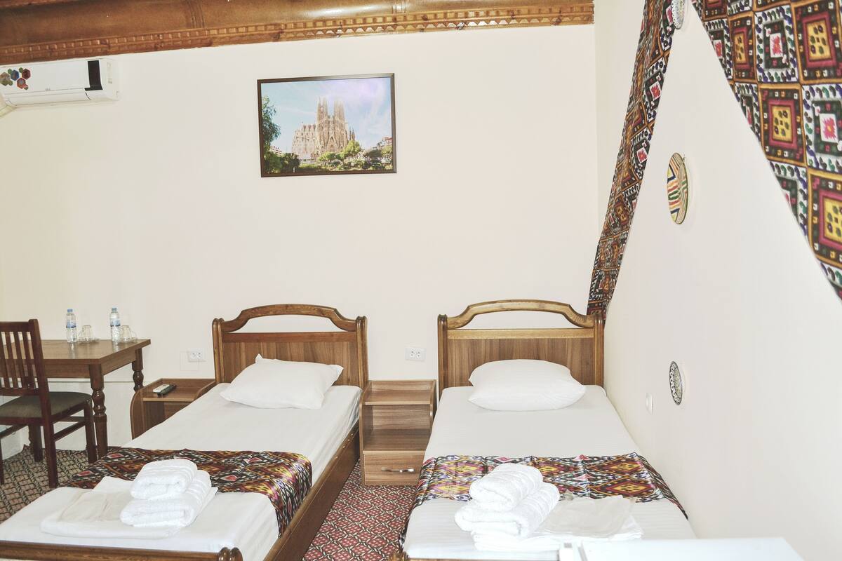 A hotel room with two single beds, a wooden desk, a chair, and a picture of a cathedral on the wall.