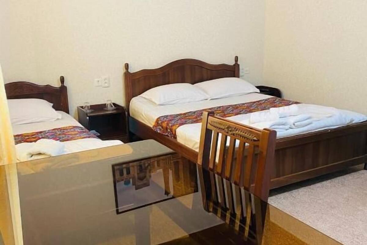 A hotel room with two beds, a wooden chair, a glass table, and a framed picture on the wall.