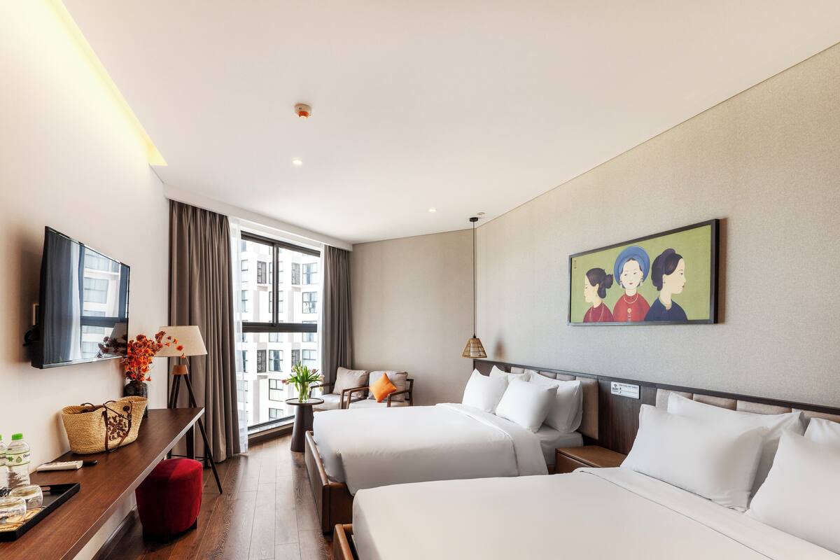 Une chambre d’hôtel avec deux lits, un bureau avec une lampe, une télévision et une fenêtre avec des rideaux.