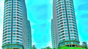 Two high-rise buildings with a dense green foliage in the foreground.