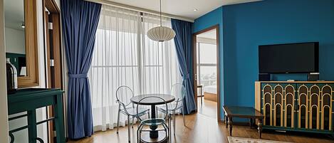 A modern hotel room with a dining area, a TV, and a view of the city.