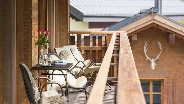 Eine Holzterrasse mit Sitzgelegenheiten im Freien, ein Tisch mit einem Blumenarrangement und ein an einem Gebäude angebrachtes Hirschschädel.