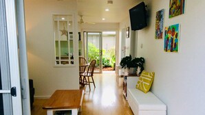 Un vaste espace de vie doté d’un plancher en bois, d’un canapé blanc agrémenté d’un coussin jaune, d’une table basse en bois et d’un coin repas avec des chaises et une table.