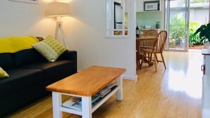 Un salon avec un canapé noir, une table basse en bois, une lampe et un coin repas comprenant une table et des chaises.