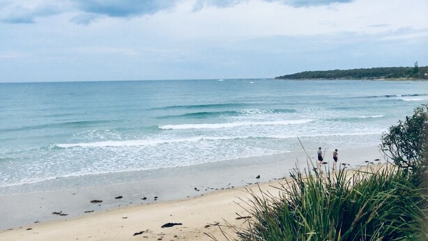 Une plage avec des vagues, une île lointaine et un ciel nuageux.