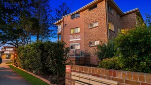 A multi-story apartment building named "The Dune Apartments" with a brick facade, a small balcony, and a well-maintained lawn area.