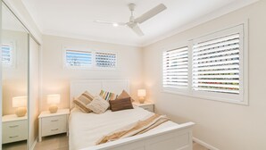A bedroom with a bed, nightstands, a ceiling fan, and windows with blinds.