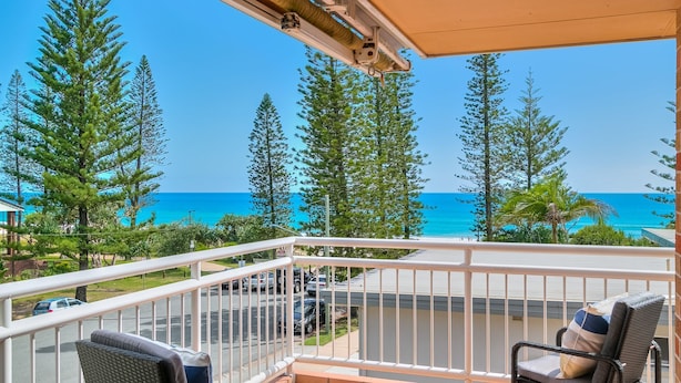 A balcony with a view of the ocean, surrounded by trees.