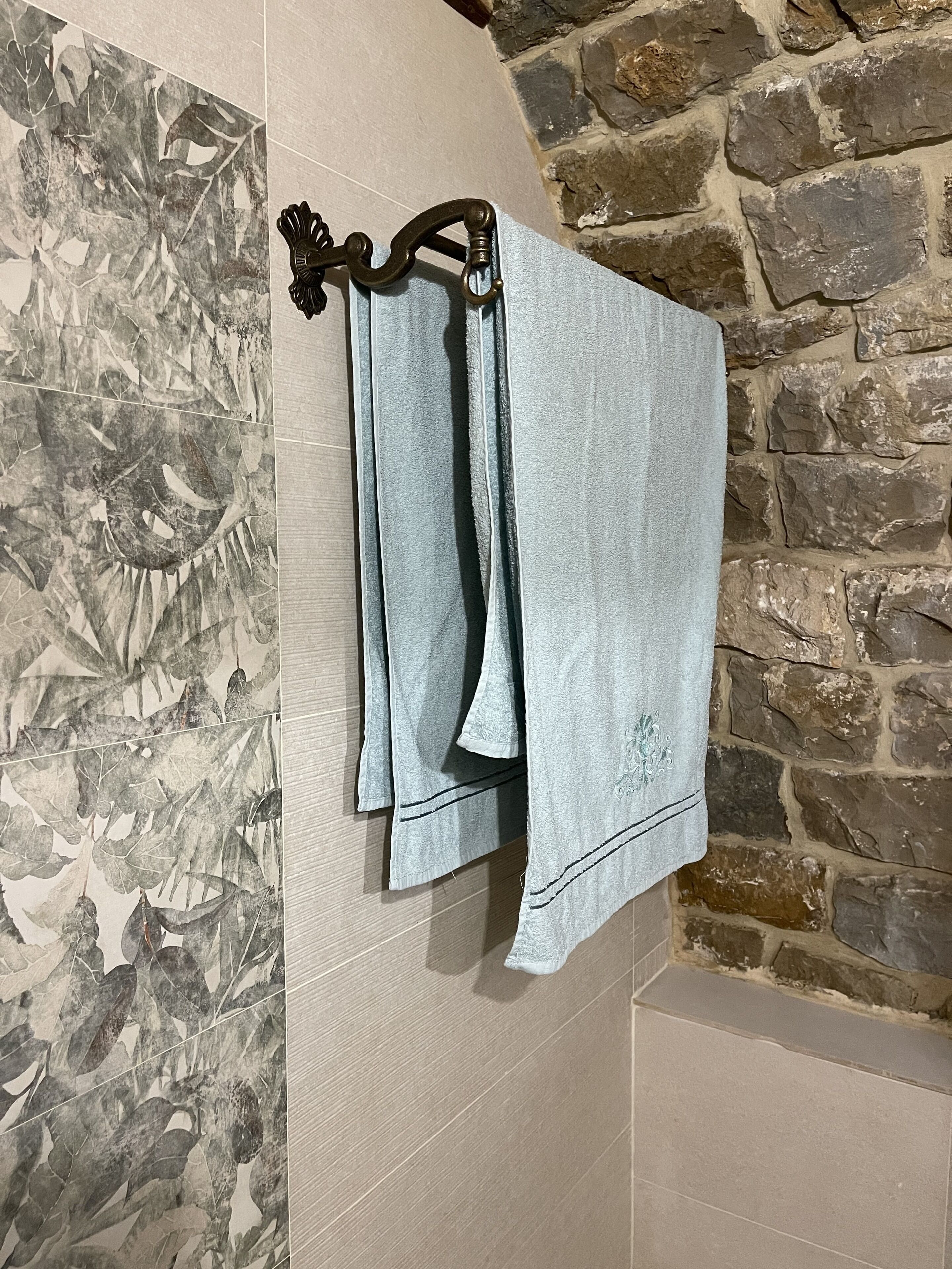 Un baño con pared de piedra, un perchero con toalla y un papel tapiz decorativo.