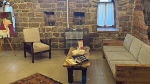 A cozy room with a stone wall, a wooden bench, a sofa, a chair, and a table with books and a lamp.