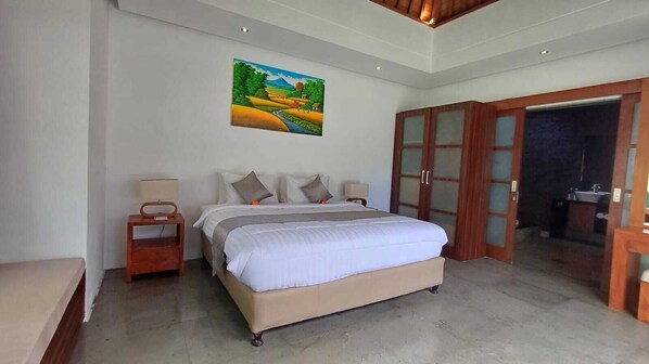 A bedroom with a large bed, a nightstand, a painting on the wall, and a wardrobe. - Villa Isabella (Seminyak)