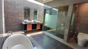 Un baño moderno con una bañera grande, dos lavamanos, una cabina de ducha de vidrio y una pared con textura de piedra.