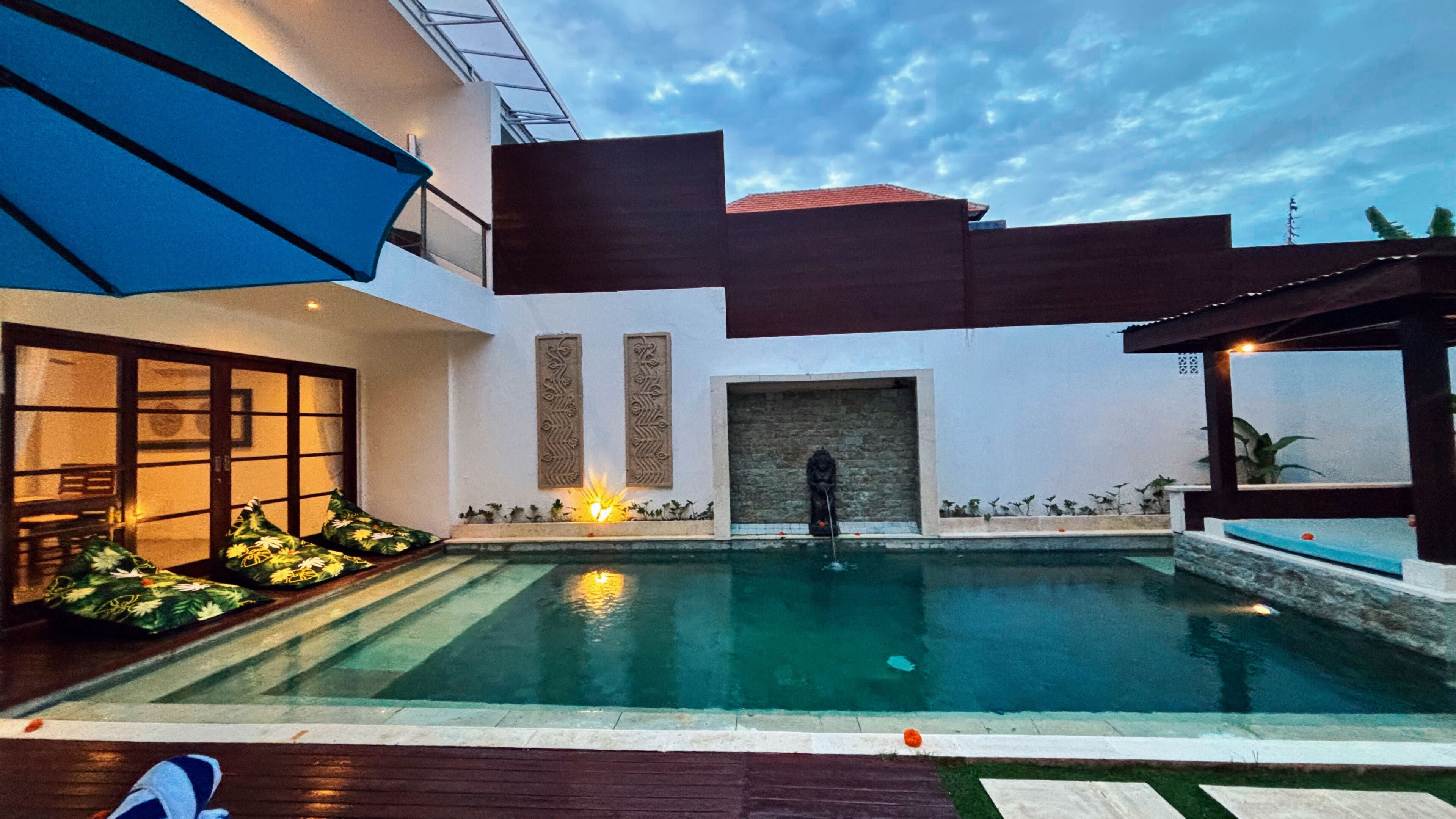 A modern pool area with a clear view of the pool, a covered seating area, and a stone wall with decorative carvings.