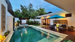 A modern outdoor pool area with a pergola, lounge chairs, and a well-maintained lawn. - Villa Isabella (Seminyak)