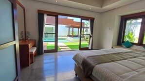 Un dormitorio con una cama grande, un banco de madera y un cristalero corredizo que da a una zona de piscina.