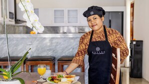 Una persona sirviendo comida en una cocina moderna con encimeras de mármol y mobiliario de madera.