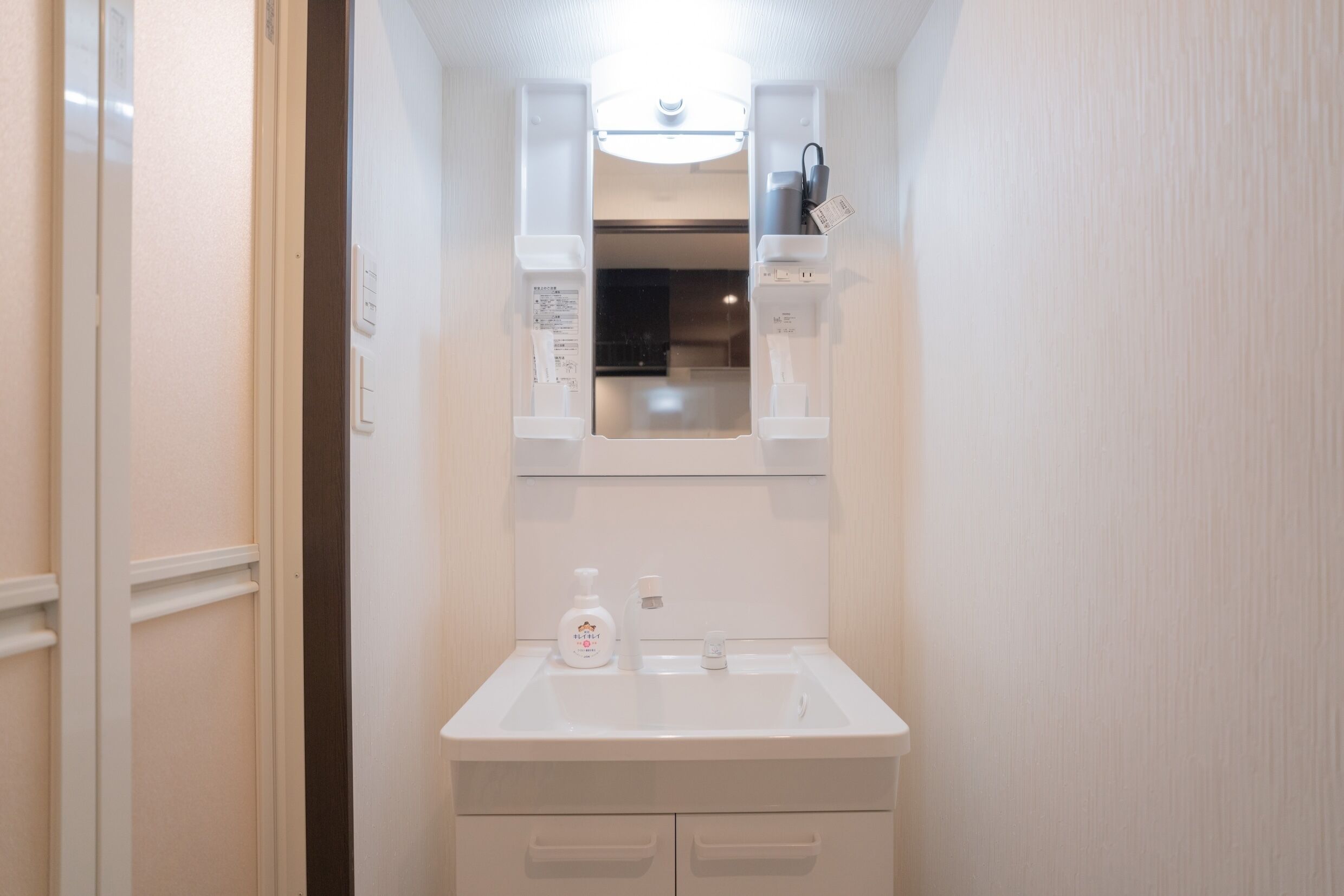 Une petite salle de bain avec un lavabo blanc, un miroir au-dessus et un flacon de savon liquide sur le comptoir.