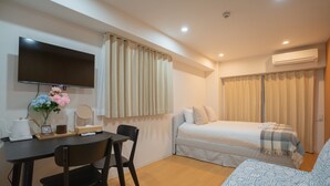 A modern room with a bed, a sofa, a TV, a table with chairs, and a window with curtains.
