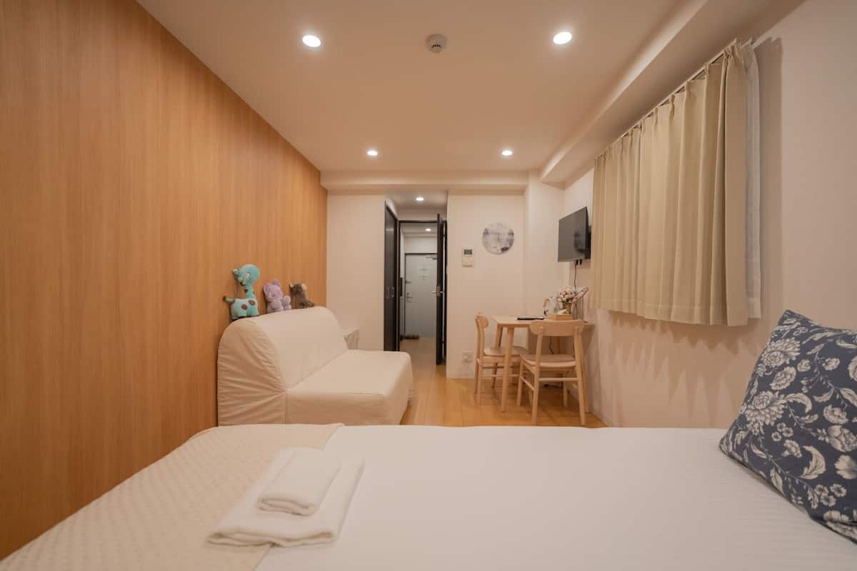 Une chambre d’hôtel avec un lit, un bureau et une chaise. Il y a un téléviseur accroché au mur et une fenêtre avec des rideaux.