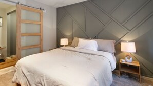 Een slaapkamer met een bed, twee nachtkastjes met lampen, een houten garderobe en een wand met een geometrisch patroon.