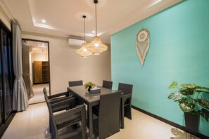 A dining area with a table and chairs, a hanging light fixture, and a wall-mounted macrame piece.