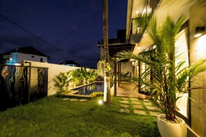 A well-lit residential area with a swimming pool, a grassy lawn, and a pathway leading to a house.