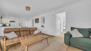 A modern living room with a brown leather sofa, a green sofa, a wooden coffee table, and a kitchen in the background. - Riverview Units - Wapengo St 5 Unit 3 (Bermagui)