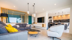 Un salon moderne avec un canapé gris, une table basse et un fauteuil de couleur gris clair. On y trouve un grand miroir et un téléviseur fixé au mur.