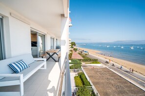 A balcony with a white sofa and a table, overlooking a beach with a clear sky and boats in the distance. - [Grand Standing] Vue Mer imprenable et accès plage (Arcachon)