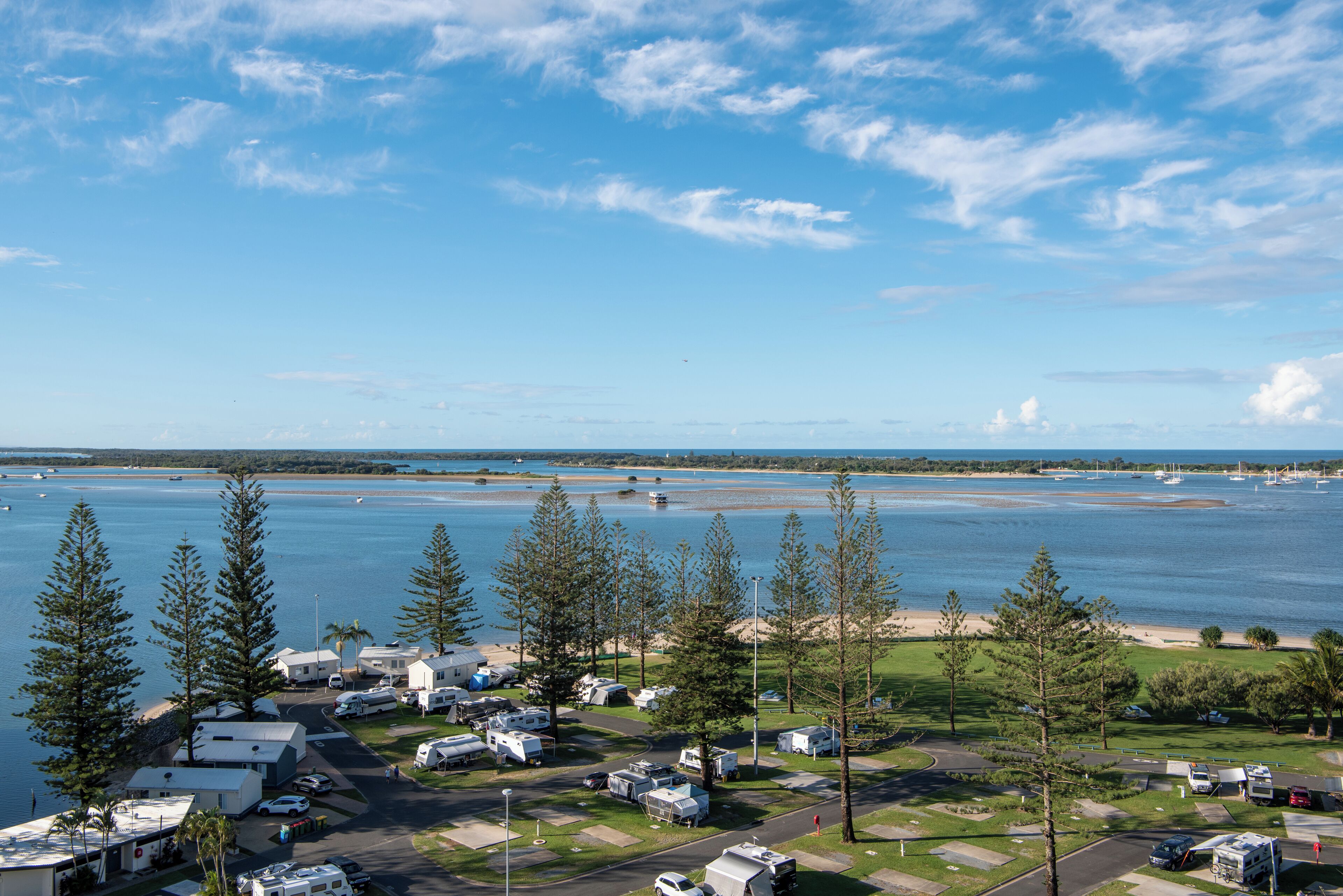 Een RV-park aan het meer met meerdere campers en aanhangwagens, een parkeerplaats en een uitzicht op het meer en boten in de verte.