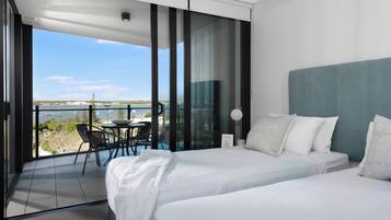 Habitación de hotel moderna con una cama grande, un balcón con mesa y sillas, y vista al mar.