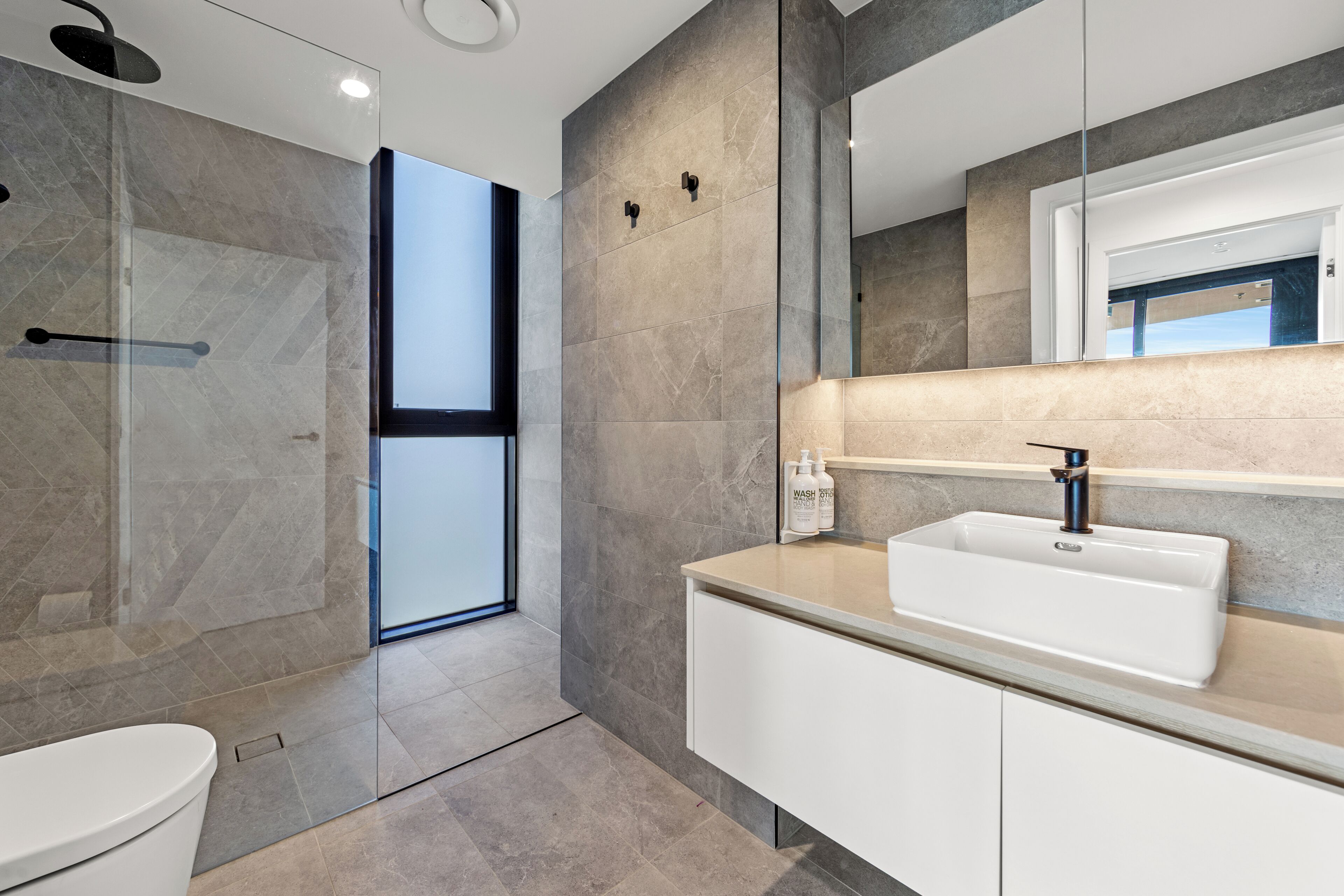 Un baño moderno con cabina de ducha de vidrio, un lavamanos blanco y un espejo grande.