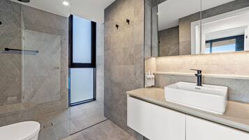 Un baño moderno con cabina de ducha de vidrio, un lavamanos blanco y un espejo grande.