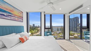 A modern bedroom with a large bed, a ceiling fan, and a city view through floor-to-ceiling windows. - Marine Quarter Apartments by CLLIX (Southport)