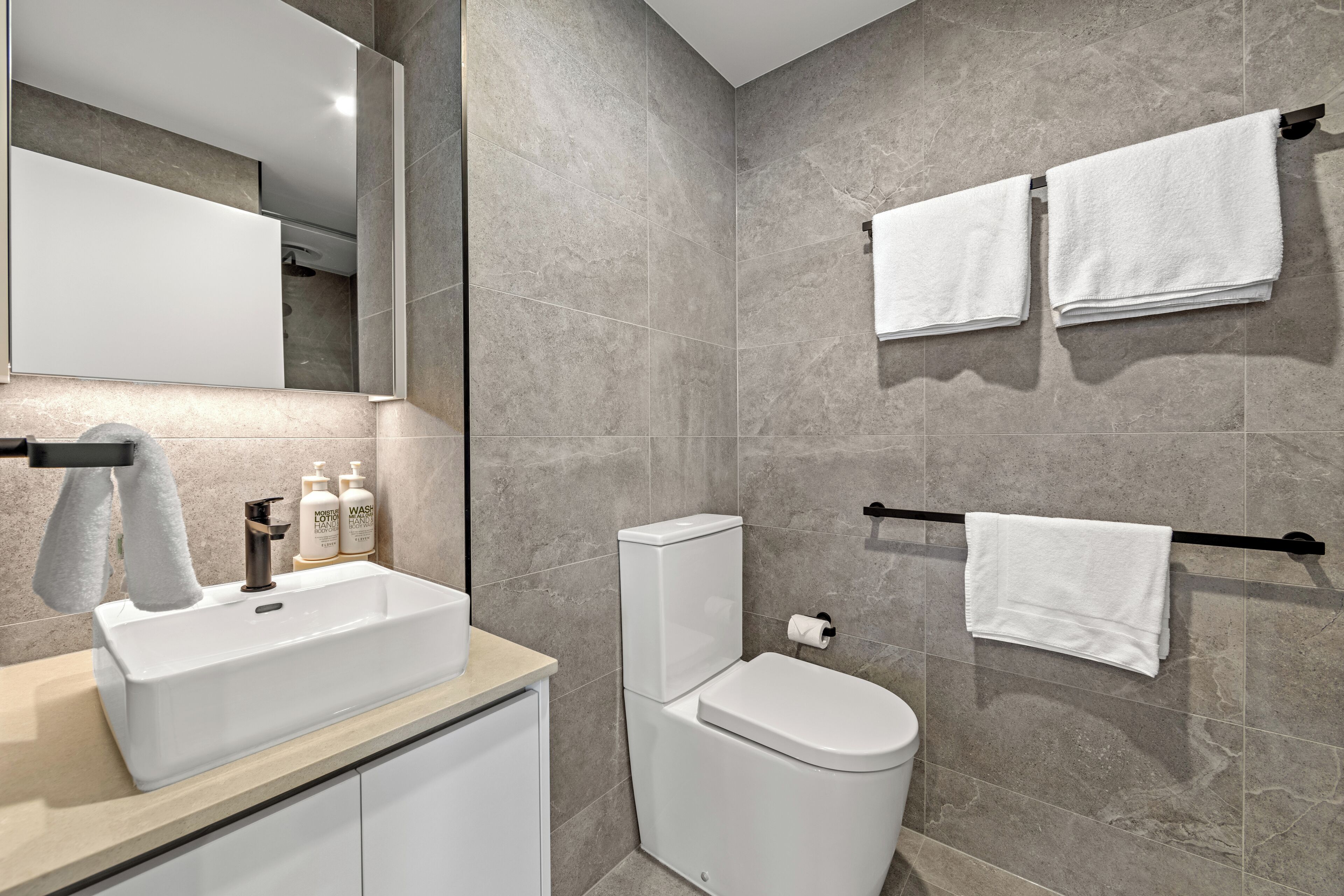 A modern bathroom with a large mirror, white sink, and two towels hanging on a towel rack.